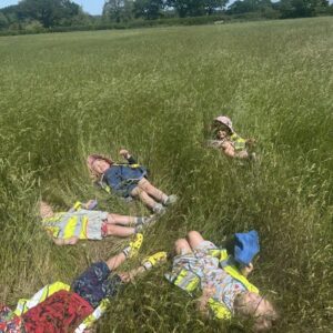 A group of children lie back in a circle in a field of tall grass.